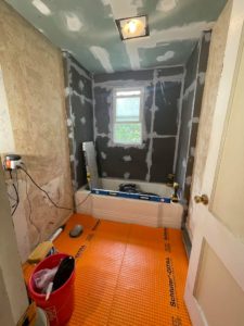 Image of bathroom remodel in progress - with tape around the bathtub and an orange floor protector. 