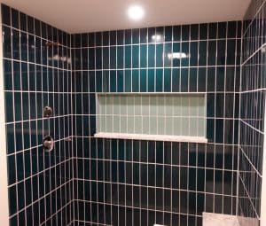 A shower with blue and white squared tile. There is also a rectangular hole in the shower for storage. 