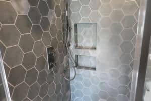 Shower with dark gray hexagonal tiles, featuring dual built-in niches and a modern matte black shower fixture, creating a sleek and contemporary look.